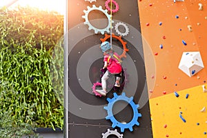 Child climbing on wall in amusement centre. Climbing training for children. Little girl in dressed climbing gear climb high.