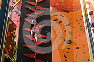 Child climbing on wall in amusement centre. Climbing training for children. Little girl in dressed climbing gear climb high.