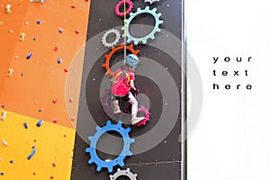 Child climbing on wall in amusement centre. Climbing training for children. Little girl in dressed climbing gear climb high.