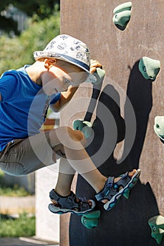 The child climbs to the top, on the climbing wall. A young mountaineer trains to climb the climbing wall