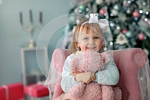 A child close up on the background of a Christmas tree hugs a Teddy bear