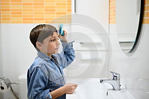 Child combs his hair in front of a mirror in the toilet of his home