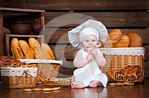 Child cooks eating a bagel on the background of baskets with rolls and bread.