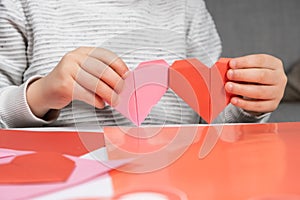 The child creates a hearts out of paper, hands close-up. Origami for Valentine& x27;s Day.