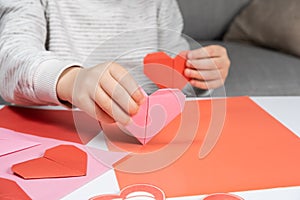 The child creates a hearts out of paper, hands close-up. Origami for Valentine& x27;s Day.