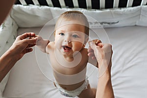 The child is in the crib. Portrait of a nine-month-old smiling baby girl standing in the playpen. Cheerful happy child