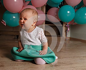 The child cries, gets angry, a little girl, a child, sits on the floor and cries, wrinkled her nose, near the balloons, a holiday.