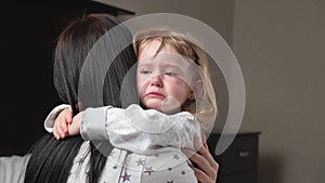 Child is crying in room in the arms of his mother. A loving young mother hugs and comforts her little daughter. Mom