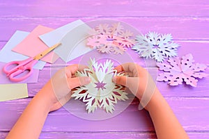 Child cut a snowflake of colored paper. Little child holds a paper snowflake in hands. Colored paper sheets, scissors, snowflake