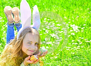 Child with cute bunny ears lying at meadow. Little girl hunting for Easter egg in spring garden on Easter day