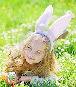 Child with cute bunny ears lying at meadow. Little girl hunting for Easter egg in spring garden on Easter day. Cute