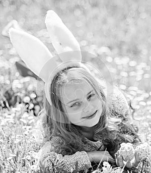 Child with cute bunny ears lying at meadow. Little girl hunting for Easter egg in spring garden on Easter day. Cute