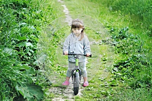 Child cute little girl riding bike in forest