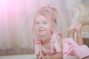 Child with cute smile in pink dress lie on carpet