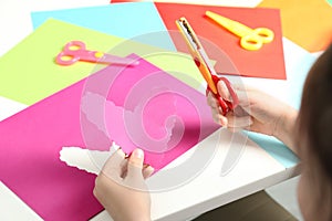 Child cutting out paper heart with craft scissors at table