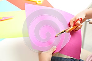 Child cutting out paper heart with craft scissors at table, closeup