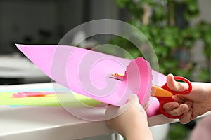 Child cutting out paper heart with craft scissors at table indoors