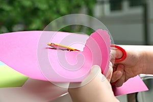 Child cutting out paper heart with craft scissors at table indoors,