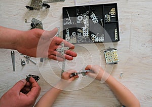 Child and  dad assemble a construction kit. Screw driver, nuts, wrench, bolts and parts of children`s metallic constructor.