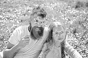 Child and dad posing with star shaped eyeglases photo booth attribute at meadow. Father and daughter sits on grass at photo