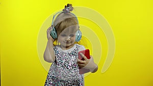 Child dances with smartphone, listening to music on headphones. Little kid girl dancing, having hun