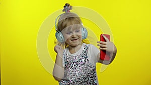 Child dances with smartphone, listening to music on headphones. Little kid girl dancing, having hun