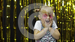 Child dancing, show amazement, fooling around, smiling. Girl posing on background with foil curtain