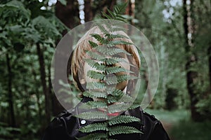 A child in a dark forest is covered by a fern leaf. Child in a black leather jacket in the forest fashionable trendy