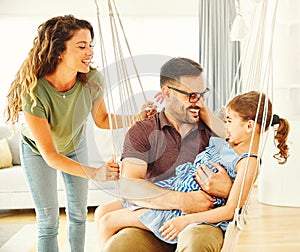 child daughter family happy mother father sofa playing fun together girl cheerful smiling home indoor swing