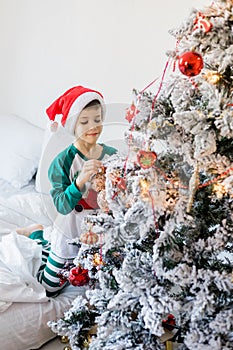 Child decorates Christmas tree. The boy is holding a Christmas toy. Morning before christmas at home. Generation alpha