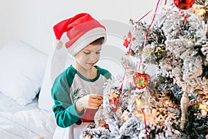 Child decorates Christmas tree. The boy is holding a Christmas toy. Morning before christmas at home. Generation alpha