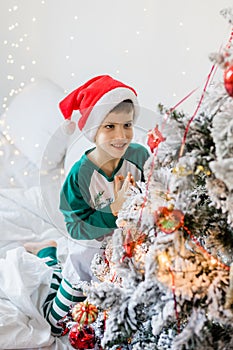 Child decorates Christmas tree. The boy is holding a Christmas toy. Morning before christmas at home. Generation alpha