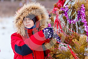 Child decorates a Christmas tree in the forest with tinsel