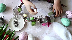 child decorates an Easter wreath with decorative eggs, wooden table with tulips