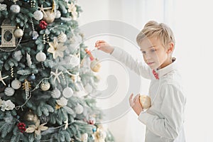 Child decorating Christmas tree at home. Boy hangs Christmas balls on tree. Christmas Eve concept