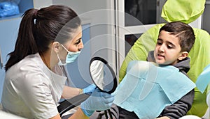 The child at the dentist in the chair shows his teeth in the mirror