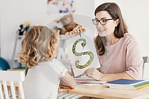 A child with development problems with a professional speech therapist during a meeting. Tutor holding a prop poster of a snake as