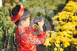 Child with digital compact camera outdoors. Cute little Vietnamese boy in ao dai dress. Tet holiday
