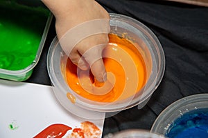 a child dipping his finger into a pot of orange paint for finger painting