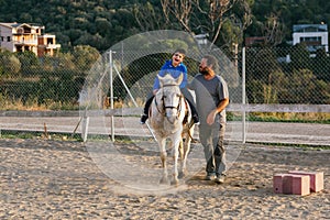 Child with disabilities riding a horse in an equine therapy session at an equestrian center.