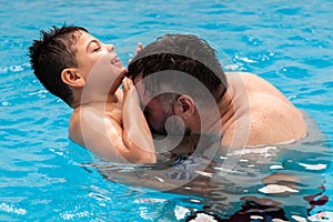 child with disability laughs and plays in his father& x27;s arms in a swimming pool
