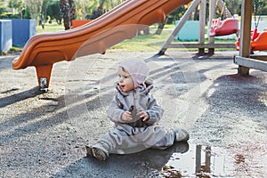 a child discovers the world, one small child in dirty clothes 1 year and 3 months old sits in a puddle on the playground