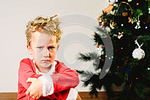 Child with disguise, anxious and sad on Christmas day with an angry face next to the Christmas tree while waiting for Santa photo