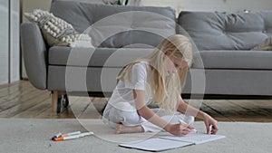 Child does homework by drawing markers on paper at home. Pretty caucasian blonde artist girl alone draws drawing with