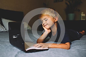 Child does homework , lying in bed using his laptop or skyping.