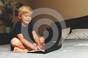 Child does homework , lying in bed using his laptop or skyping.