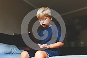 Child does homework , lying in bed using his laptop or skyping.