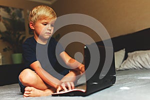 Child does homework , lying in bed using his laptop or skyping.