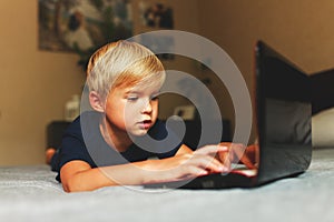 Child does homework , lying in bed using his laptop or skyping.