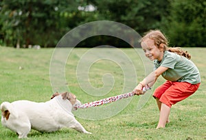 Child and dog playing tug with toy rope at backyard lawn